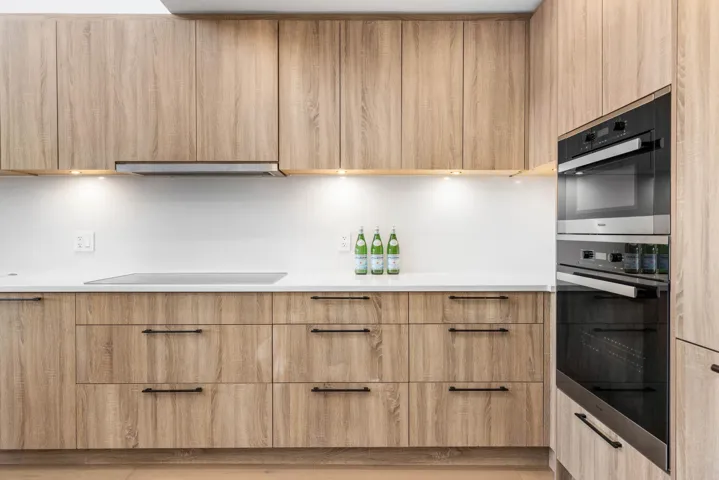 Kitchen featuring dobule oven black, under cabinet range hood, light brown cabinets, and modern cabinets