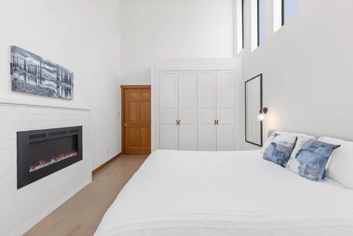 Bedroom featuring a closet, a high ceiling, a glass covered fireplace, and wood finished floors