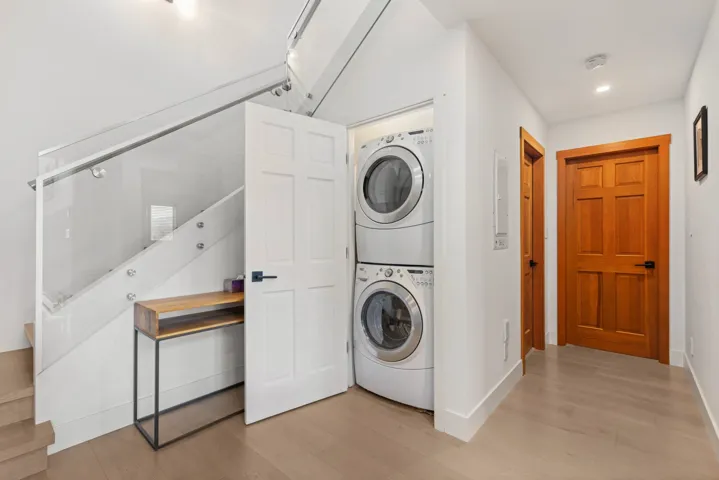 Laundry area with laundry area, stacked washer and clothes dryer, baseboards, and light wood-type flooring