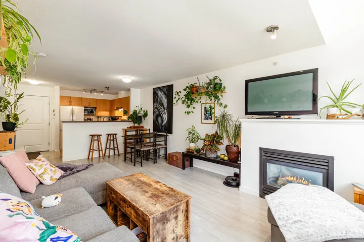 Open-concept living area with wood-finish flooring, a fireplace, and an integrated kitchen featuring light wood cabinetry