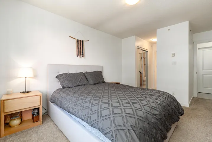 Carpeted room featuring a white upholstered headboard and light wood-finish nightstand