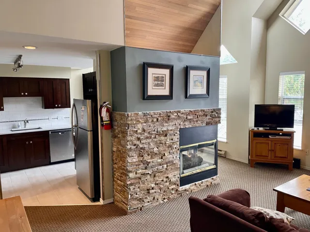 Living area with a fireplace, light colored carpet, and high vaulted ceiling