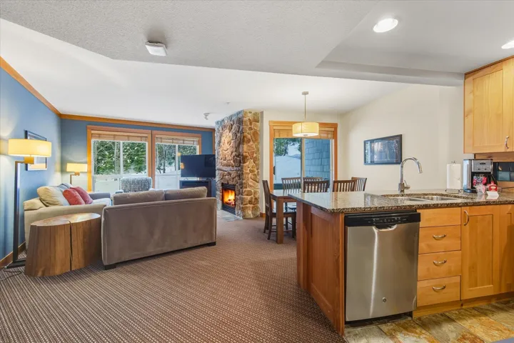 Kitchen featuring dark stone counters, dishwasher, a peninsula, a stone fireplace, and open floor plan