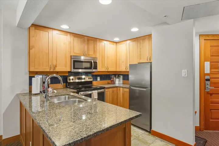 Kitchen with appliances with stainless steel finishes, dark stone counters, a peninsula, tasteful backsplash, and recessed lighting