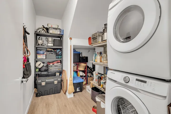 Washroom with light wood-type flooring and stacked washer / drying machine