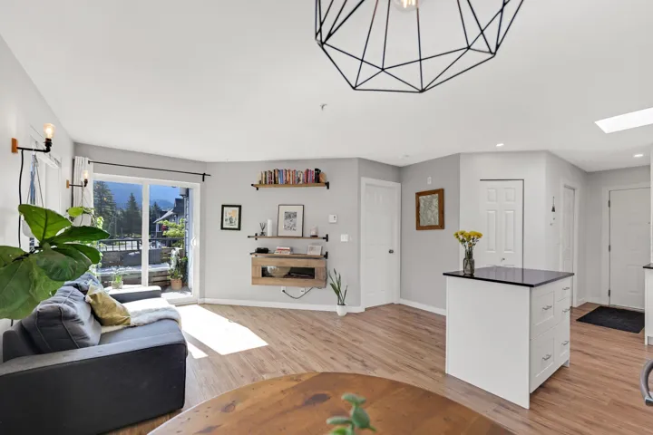 Open-concept living area featuring wood-finish flooring, a contemporary geometric ceiling light fixture, and a kitchen island with a black countertop