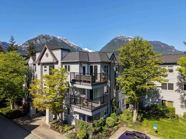 Multi-story residential building featuring light grey siding, dark grey trim, and multiple private balconies with black railings
