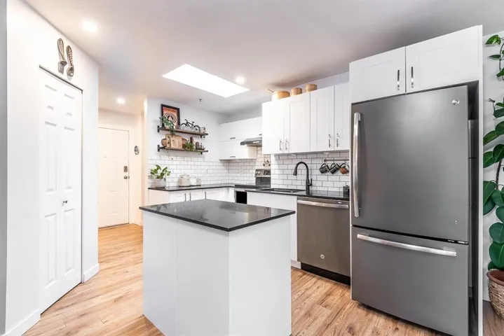 Modern kitchen featuring white shaker cabinetry, dark countertops, white subway tile backsplash, and wood-finish flooring