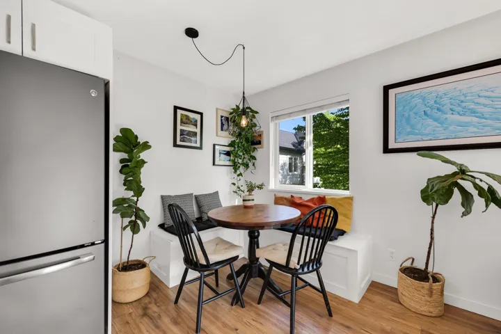 Compact dining area featuring a built-in bench seating, wood-finish flooring, a large window, and a stainless steel refrigerator