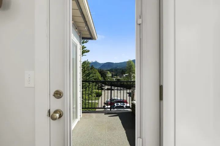 Balcony access through a white door, featuring a black metal railing and concrete flooring