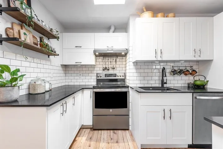 Modern kitchen featuring a central island with a dark countertop, stainless steel appliances, white cabinetry, wood-finish flooring, and a skylight