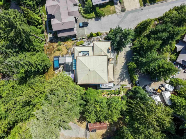 Property featuring a distinct roofline, surrounded by dense mature trees, an outdoor swimming pool, and a glass-enclosed structure