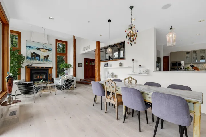 Open-concept living space featuring wood-finish flooring, a fireplace with a wood mantel, and tall windows with wood trim