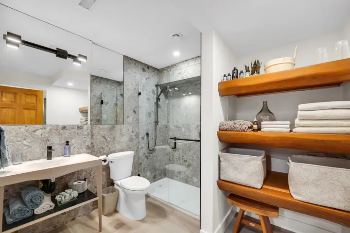 Contemporary bathroom featuring a walk-in shower with glass enclosure, a floating vanity with a vessel sink, a wall-mounted mirror, modern light fixtures, and integrated wood shelving