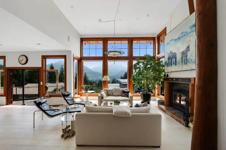 Living area featuring large wood-framed windows, a prominent wood-burning fireplace with a log mantel, and light wood-finish flooring