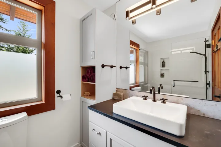 Bathroom featuring a vessel sink with dark bronze fixtures, a large mirror, and a frosted window with wood trim