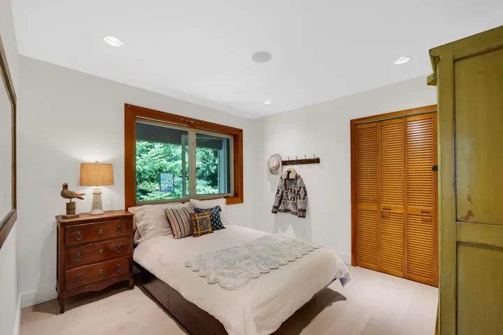 Bedroom featuring light wood-finish flooring, a large window with wood trim, recessed lighting, and a louvered bi-fold closet door