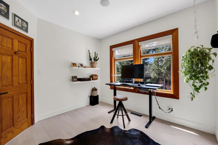 Bright room with light wood-finish flooring, featuring a warm-toned wooden door, white baseboards, and two windows with natural wood trim