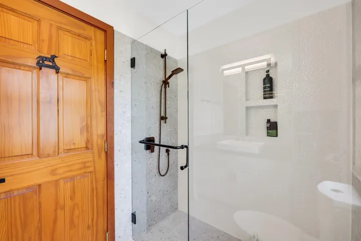 Walk-in shower featuring a frameless glass enclosure, dark bronze fixtures, and textured wall tiling
