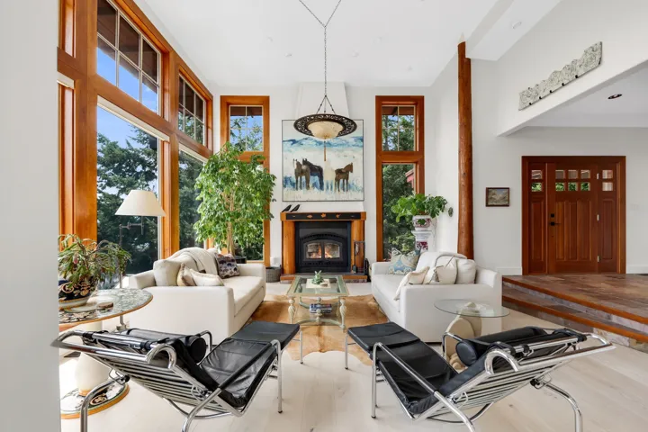 Spacious living area featuring expansive floor-to-ceiling windows with wood frames, a central fireplace with a dark mantel, and light-tone wood-finish flooring