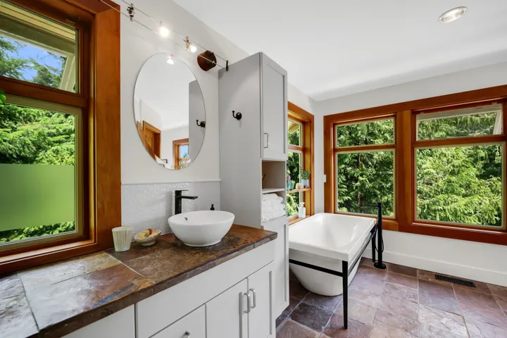 Bathroom featuring a freestanding tub, wood-trimmed windows, a vessel sink, a stone-finish countertop, and slate-finish floor tiling