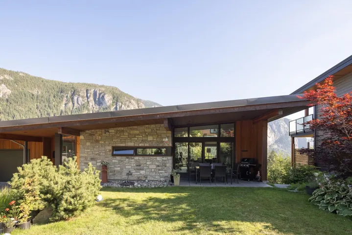 Rear view of house with a yard, a mountain view, a patio area, and stone siding