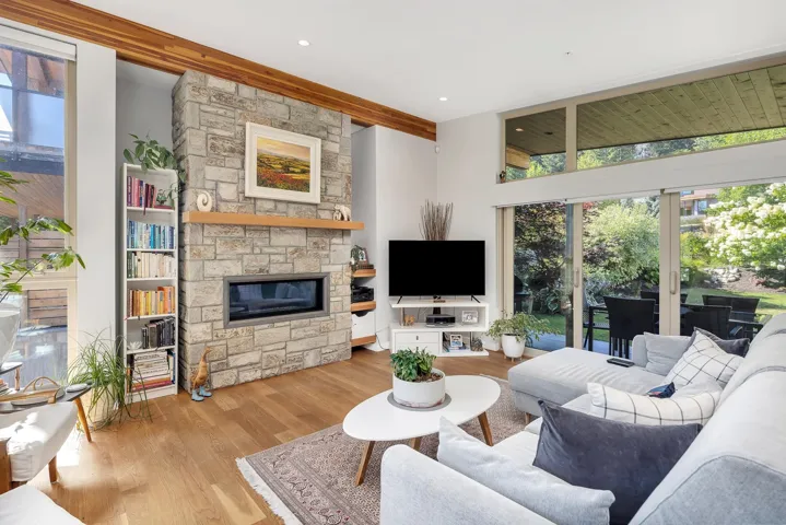 Living area featuring wood finished floors, a stone fireplace, and beam ceiling