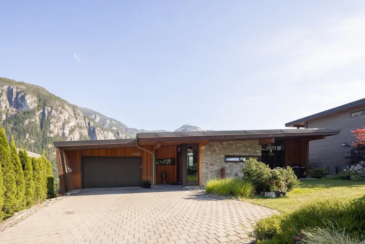 Modern home featuring stone siding, a garage, decorative driveway, and board and batten siding