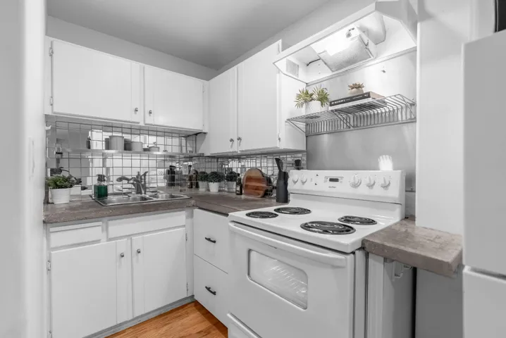 Kitchen featuring white appliances, white cabinets, decorative backsplash, wall chimney range hood, and open shelves