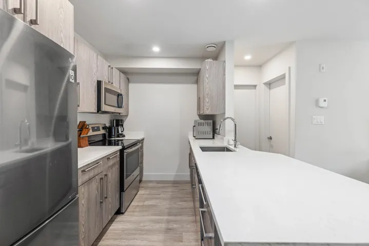 Kitchen featuring stainless steel appliances, a sink, light countertops, light wood finished floors, and a peninsula