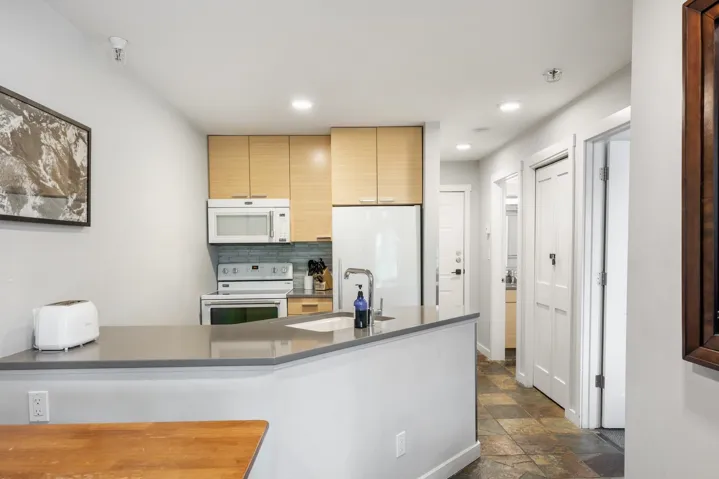 Kitchen featuring stone tile flooring, white appliances, decorative backsplash, recessed lighting, and a peninsula