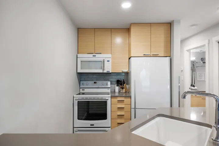 Kitchen with white appliances, decorative backsplash, and light brown cabinetry