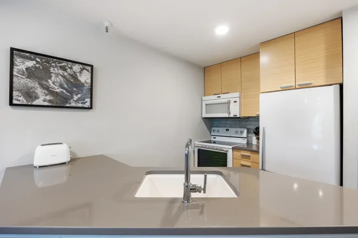 Kitchen with white appliances, tasteful backsplash, light brown cabinetry, and dark stone countertops