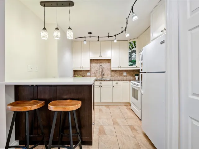 Kitchen featuring a kitchen bar, white appliances, backsplash, a sink, and white cabinets