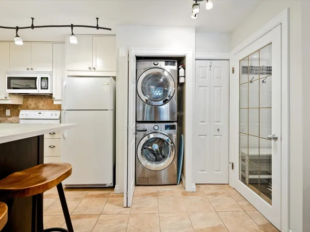 Washroom with light tile patterned flooring, stacked washer and clothes dryer, and laundry area