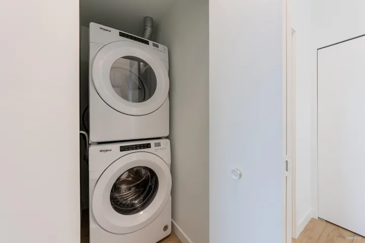 Washroom featuring stacked washer / drying machine and light wood finished floors