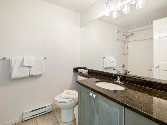 Bathroom with tile patterned floors, toilet, vanity, a baseboard radiator, and a shower