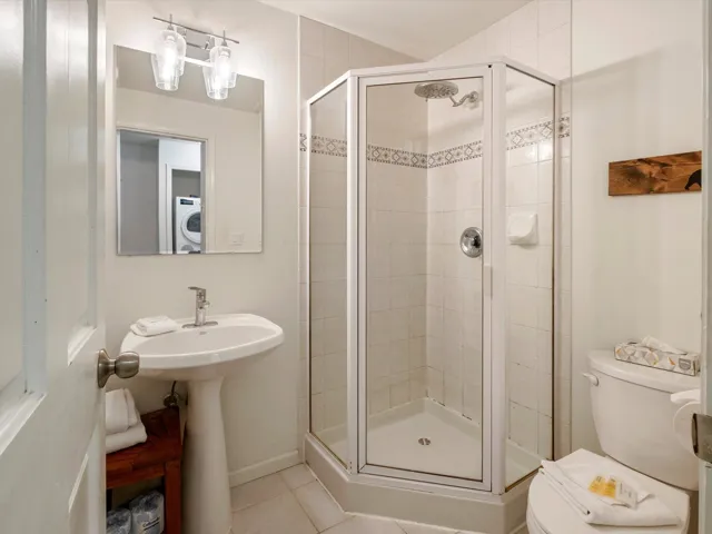 Bathroom with a shower stall, tile patterned floors, toilet, a sink, and washer / dryer
