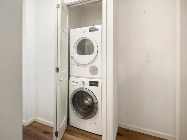Laundry area featuring stacked washer / drying machine, wood finished floors, baseboards, and laundry area