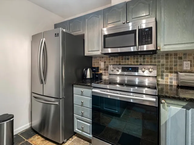 Kitchen featuring dark stone counters, stone tile floors, baseboards, backsplash, and appliances with stainless steel finishes