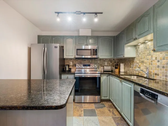 Kitchen with stainless steel appliances, a sink, backsplash, and green cabinetry