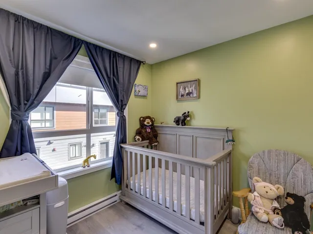 Bedroom with baseboard heating, a crib, wood finished floors, and recessed lighting