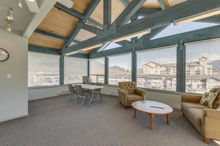 Sunroom / solarium common room with carpet flooring, a healthy amount of sunlight, vaulted ceiling with beams.