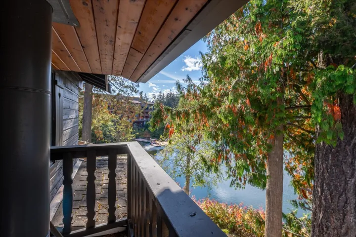 Balcony with wood plank ceiling, dark wood-tone railing, and waterfront scenery framed by mature trees