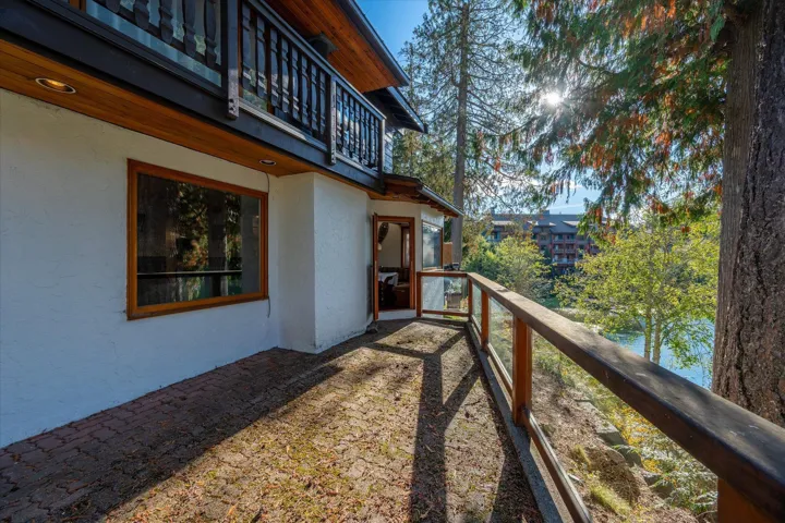 Waterfront terrace with wood-framed glass railing, brick-paved patio, and mature trees