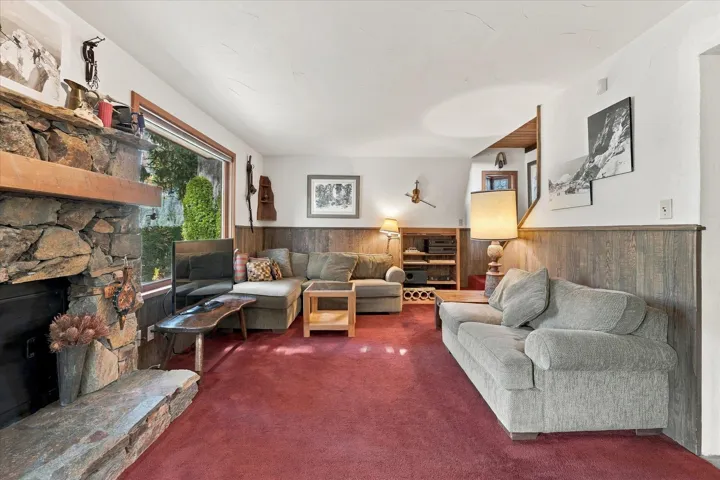 Stone fireplace with a wood mantel, stone hearth, picture window, and wood paneling