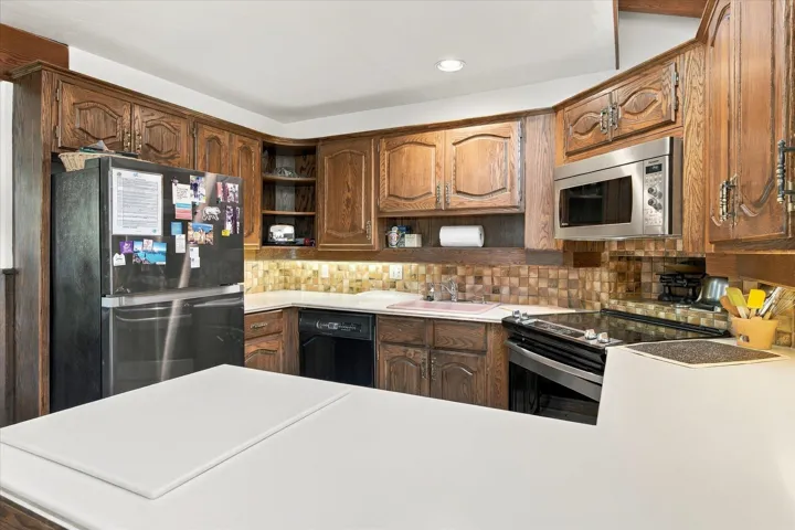 Wood-finish cabinetry and trim, stainless steel appliances, mosaic tile backsplash, and white countertops