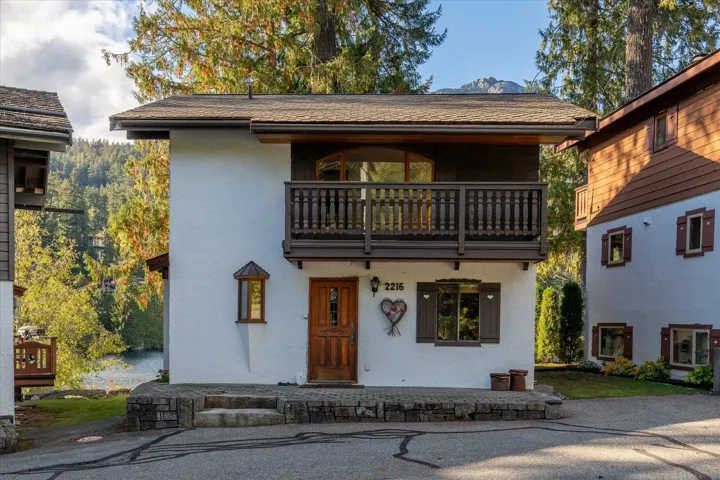 Stucco exterior with wood trim accents, a second-story balcony with balustrade, and a prominent wood-paneled entry door