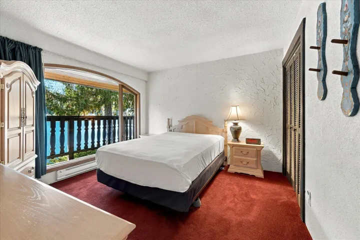 Spacious room featuring red carpeting, textured white walls, an arched window, and a balcony with wood railing