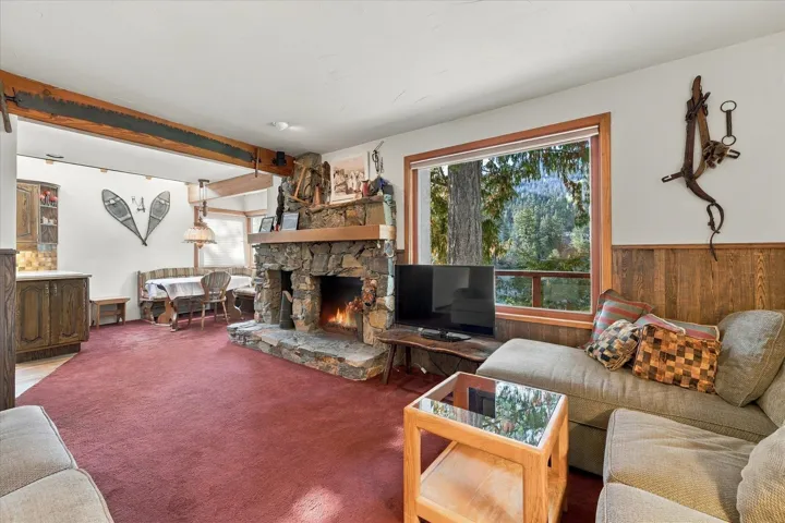 Stone-clad fireplace with a hearth, wood-paneled walls, and exposed wood ceiling beams